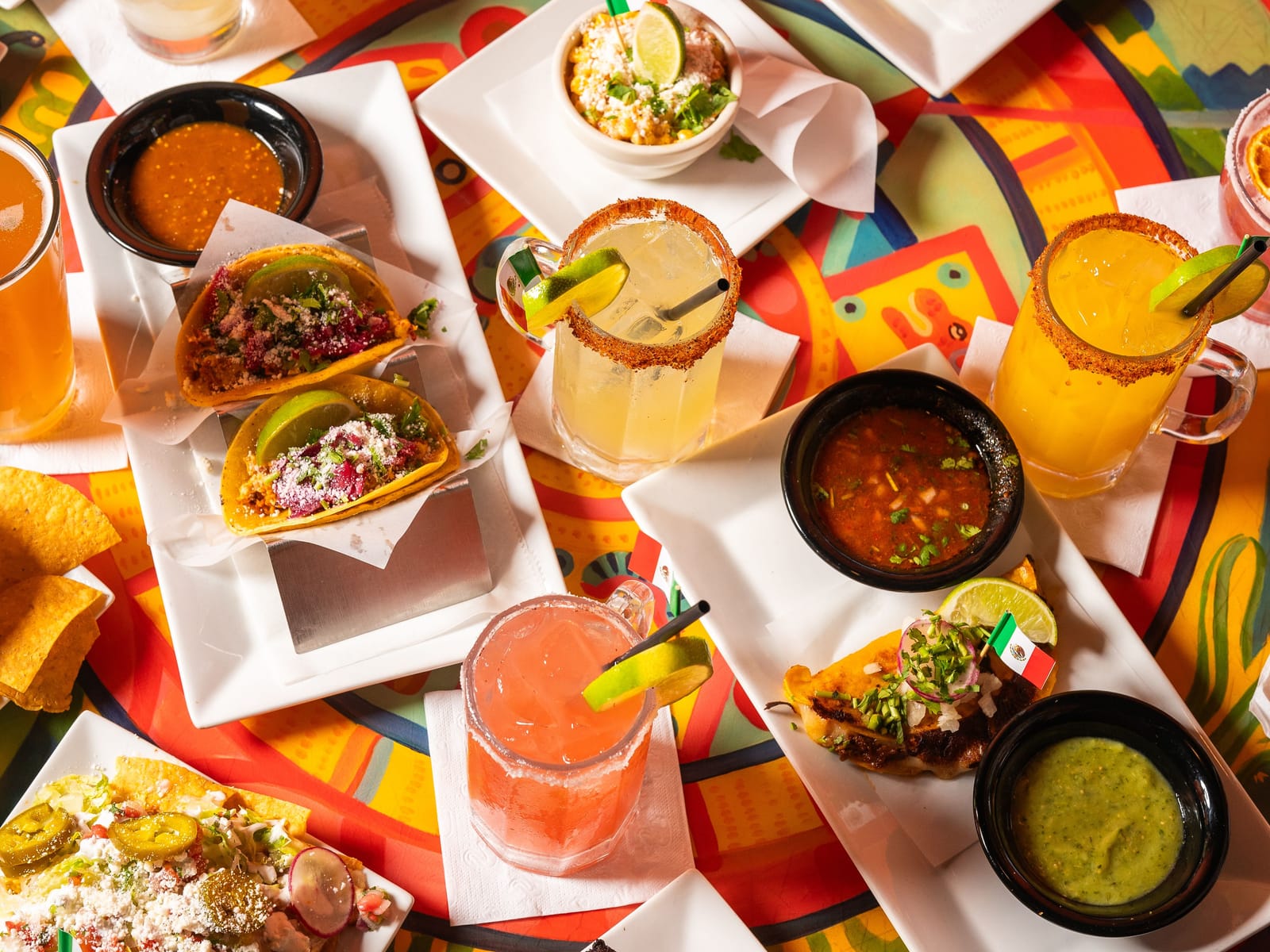 Tacos, salsas and handcrafted margaritas on a painted table, seen from above