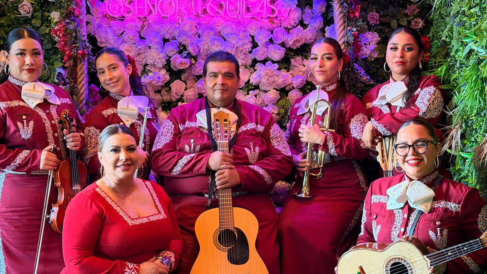 A seven-piece mariachi in black and silver charro suits playing between the tables