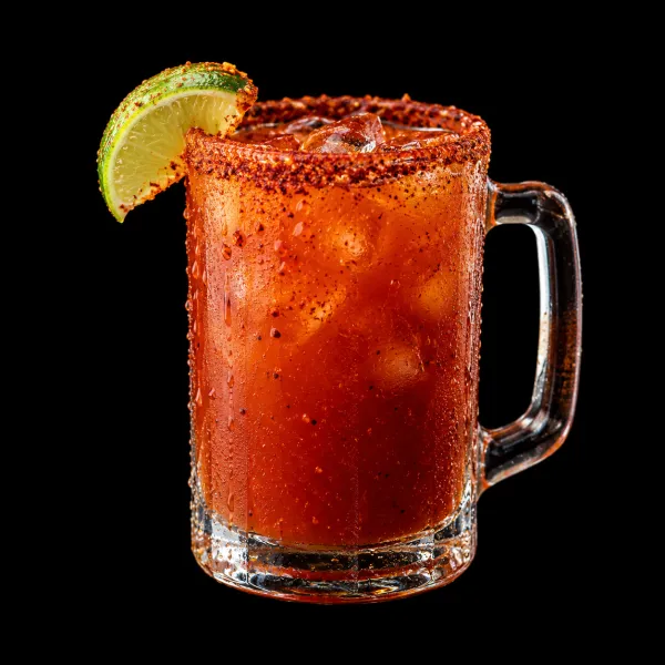 A michelada in a glass mug with a chili-salt rim and a lime wedge, on ice