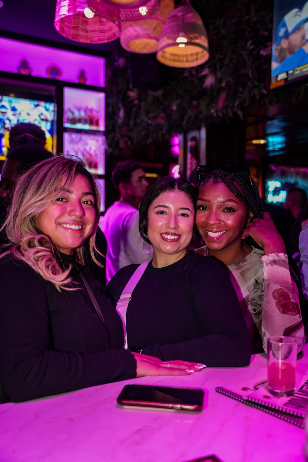 Three friends smiling together at a high table in the bar area
