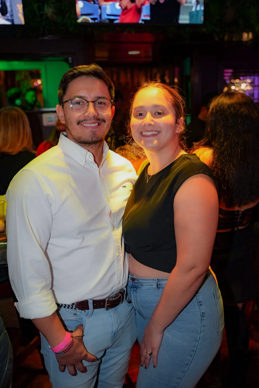 A couple smiling together in the bar area, the screens glowing behind them