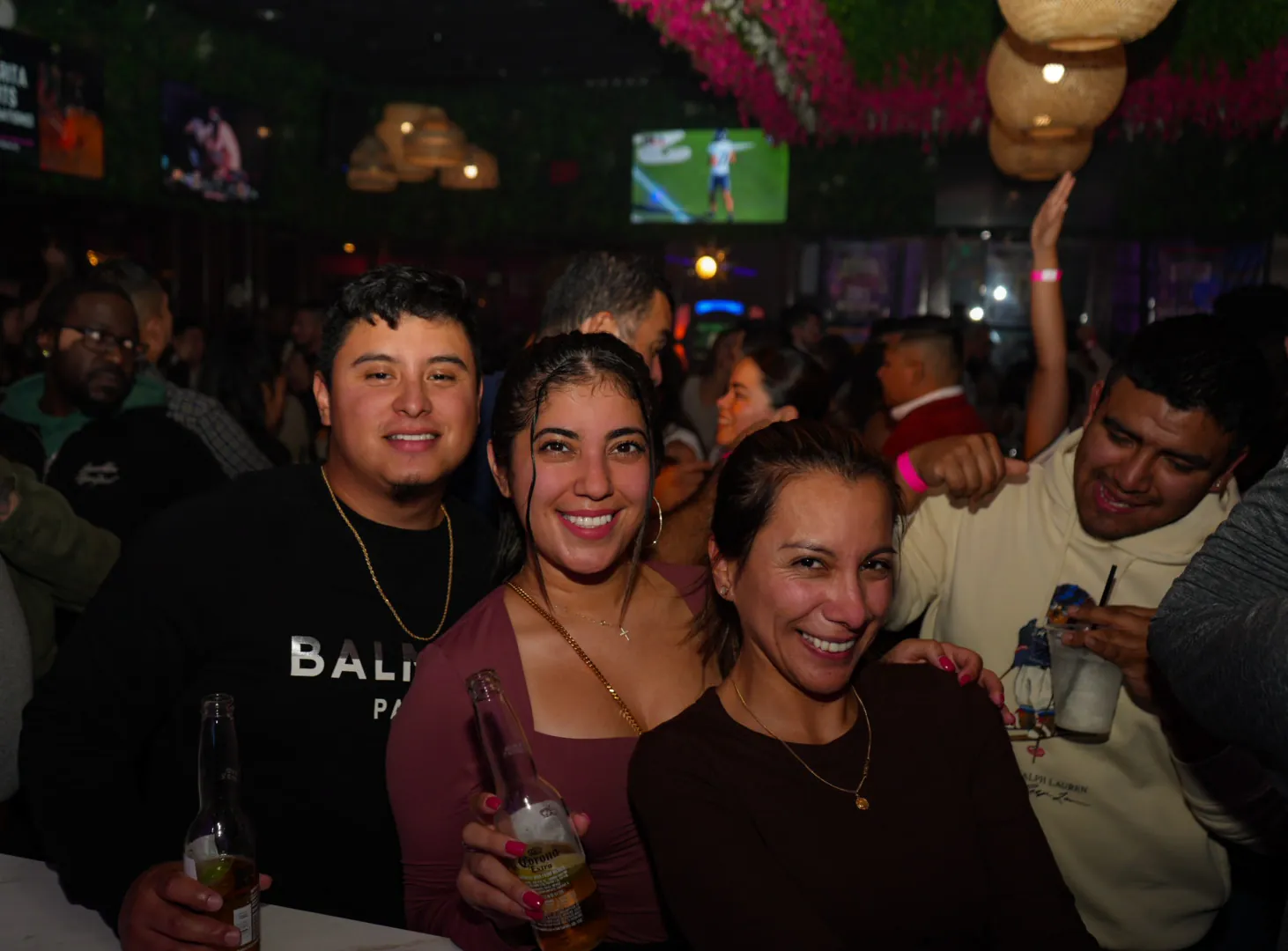 Four friends in the packed bar area raising their drinks under the flower ceiling