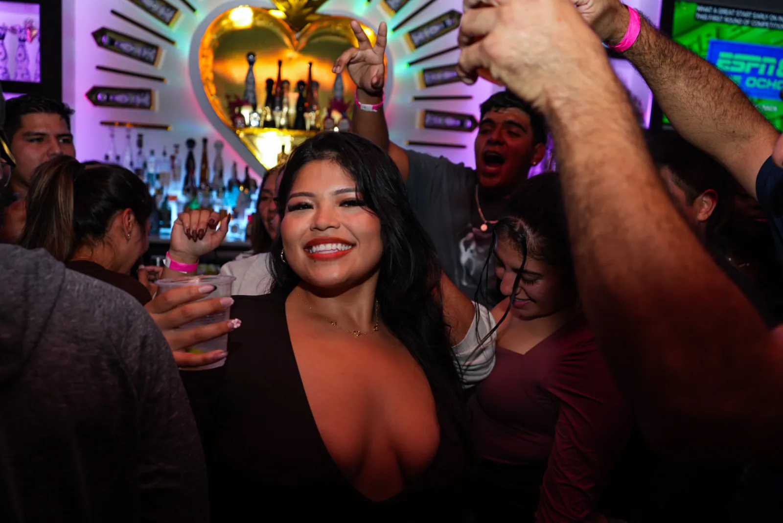 A crowd with hands in the air in front of the golden heart behind the bar