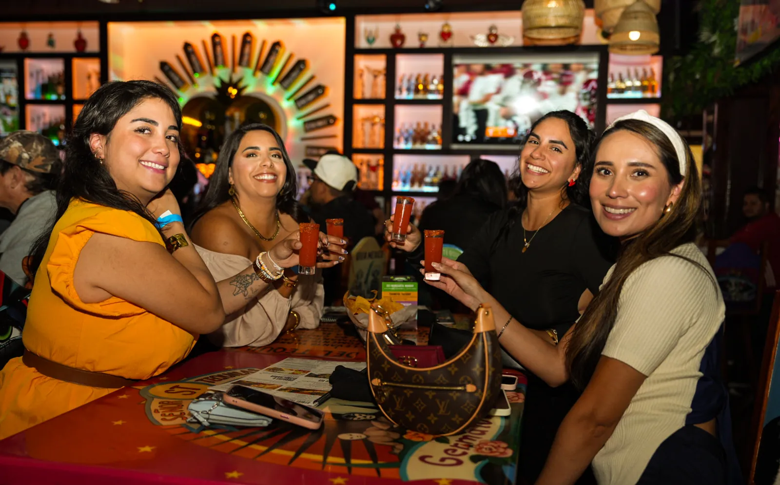 Four friends at a table holding up shooters in front of the bar