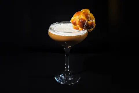 The Dulce Descanso from the side: a coffee-colored layer under the sugar-dusted foam, the mini pan de muerto perched on the rim