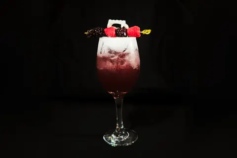 The Berry Scary in a tall wine glass, red fading up into white foam, with the berry and fang skewer across the rim