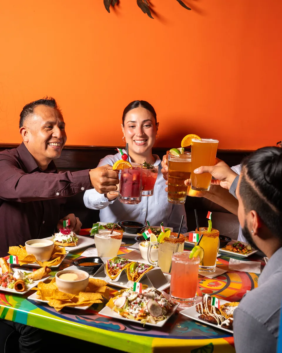 Four guests raising their glasses over a table of happy hour plates