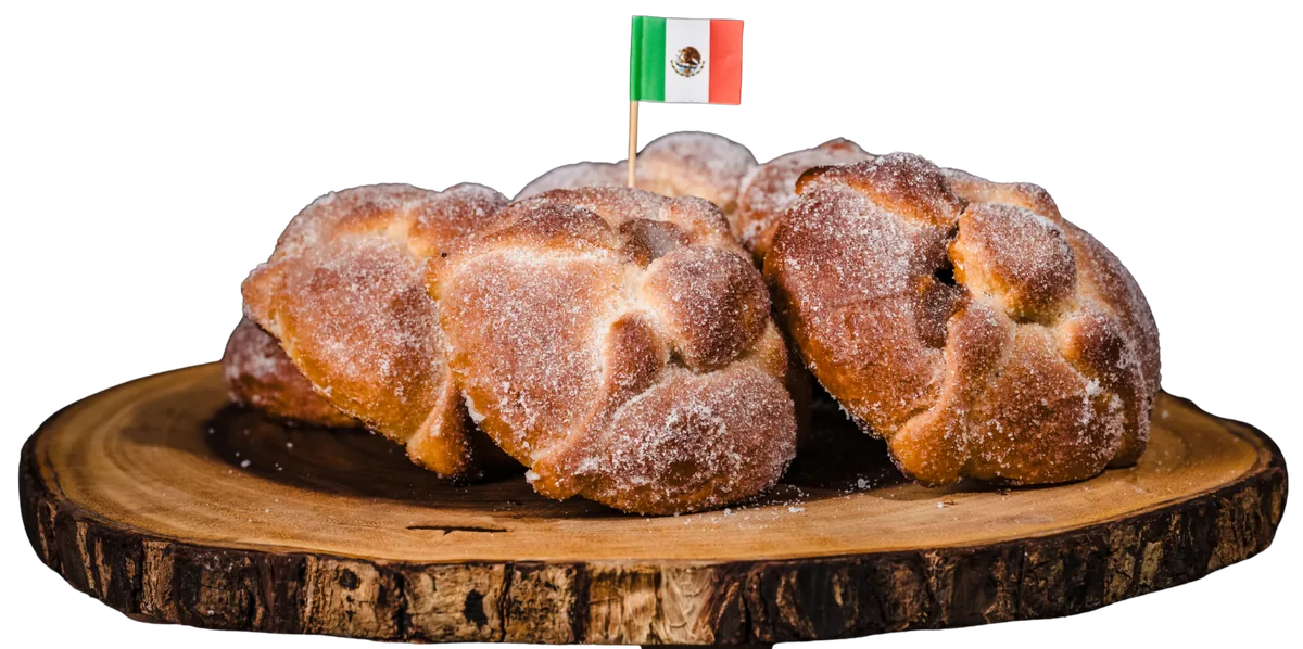 Sugar-dusted pan de muerto on a wooden board with a small Mexican flag