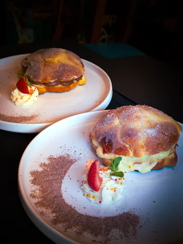 Two filled pan de muerto desserts on white plates, one chocolate cream and one vanilla cream