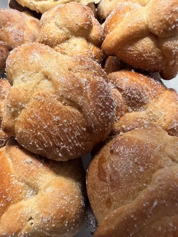 A tray of freshly baked pan de muerto under a heavy dusting of sugar