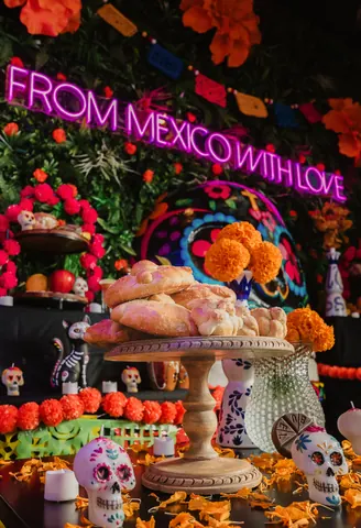 Pan de muerto on a cake stand at the Día de Muertos altar, beneath the From Mexico With Love neon sign