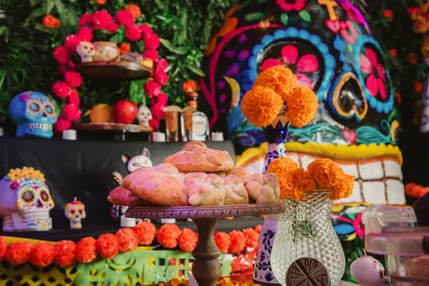 Pan de muerto on a cake stand among marigolds and sugar skulls at the Día de Muertos altar